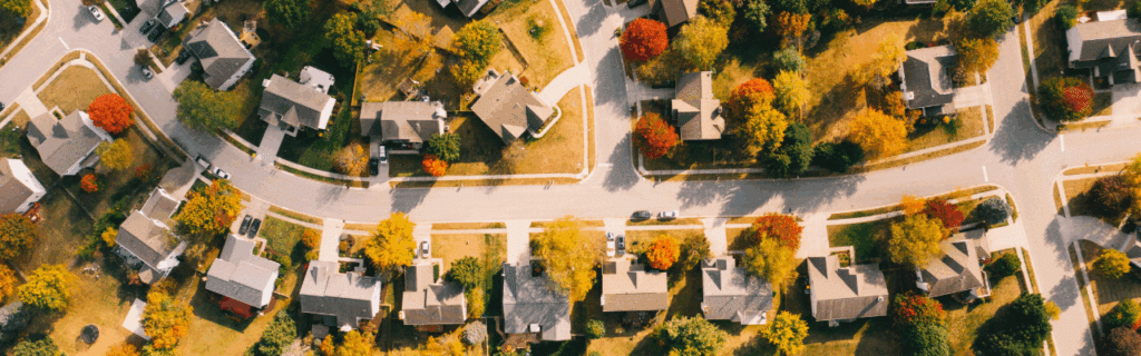 Aerial view of a suburban neighborhood with tree-lined streets and houses surrounded by colorful autumn foliage.