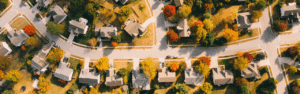 Aerial view of a suburban neighborhood with tree-lined streets and houses surrounded by colorful autumn foliage.