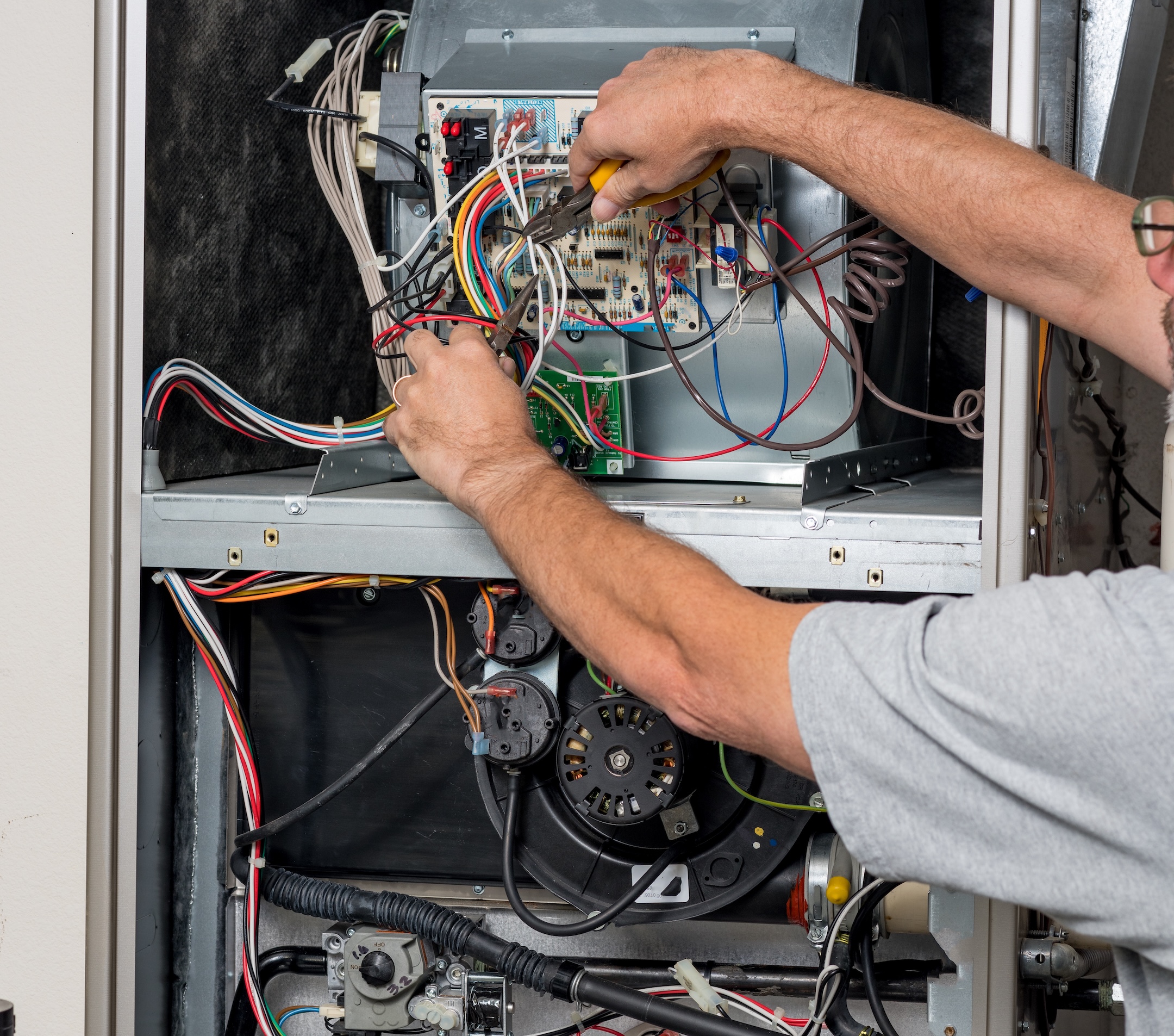 Man works with the wires on circuit boards of a home furnace