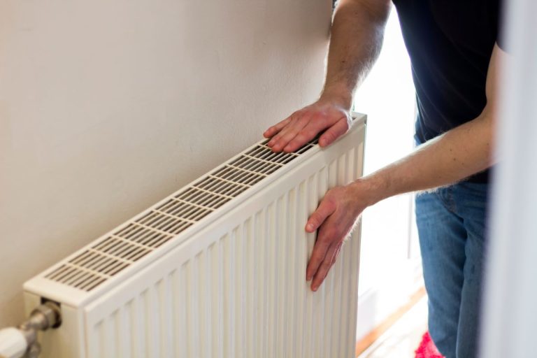 Man is checking radiator is it heating. Man warming his hands on the radiator. Home central heating system.