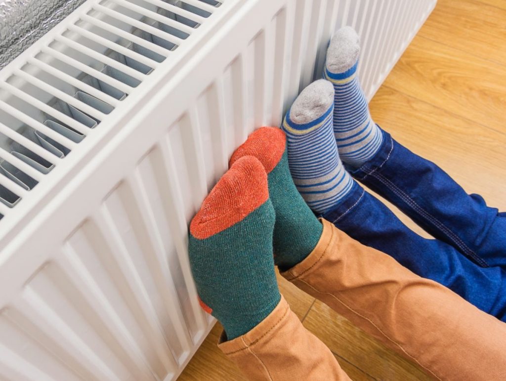 Woman-and-child-wearing-colorful-pair-of-woolly-socks-warming-cold-feet-in-front-of-heating-radiator